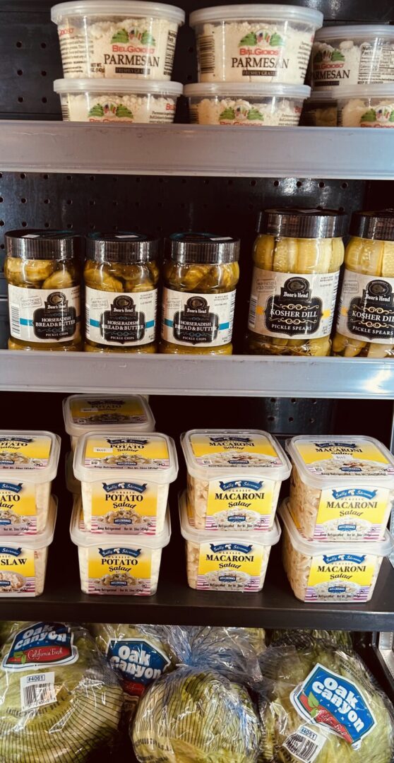 A shelf with jars of pickles and cheese.